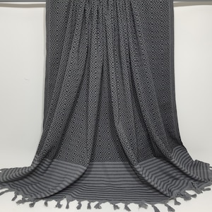 May include: A gray and black patterned beach towel with fringe. The towel has a geometric pattern and a striped border.
