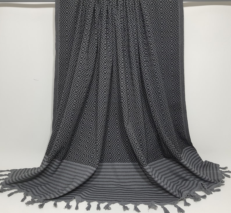 May include: A gray and black patterned beach towel with fringe. The towel has a geometric pattern and a striped border.