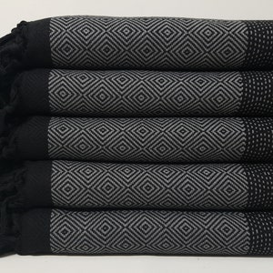 May include: A stack of five black and gray patterned towels with fringe. The towels have a diamond pattern and are folded neatly.