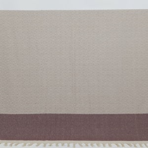 K&ouml;nnte beinhalten: Eine gewebte Wolldecke in Beige und Braun mit Fransenrand. Die Decke hat ein dezentes Rautenmuster.