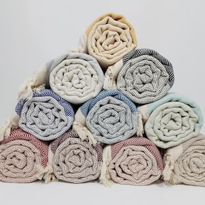 K&ouml;nnte beinhalten: Eine Sammlung von zehn gerollten t&uuml;rkischen Handt&uuml;chern in verschiedenen Farben und Mustern, darunter Beige, Blau, Gr&uuml;n, Rot und Schwarz. Die Handt&uuml;cher sind in Pyramidenform angeordnet.