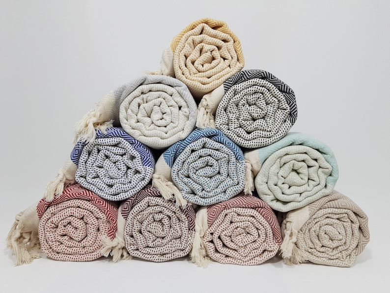 K&ouml;nnte beinhalten: Eine Sammlung von zehn gerollten t&uuml;rkischen Handt&uuml;chern in verschiedenen Farben und Mustern, darunter Beige, Blau, Gr&uuml;n, Rot und Schwarz. Die Handt&uuml;cher sind in Pyramidenform angeordnet.