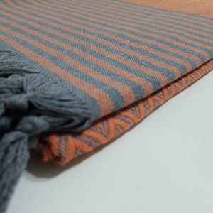 May include: A folded gray and orange striped beach towel with fringe tassels. The towel is made of cotton and has a soft, absorbent texture.