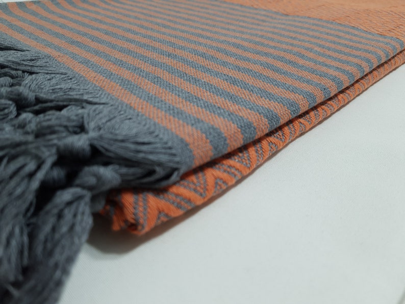 May include: A folded gray and orange striped beach towel with fringe tassels. The towel is made of cotton and has a soft, absorbent texture.