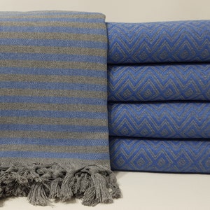 May include: A stack of blue and gray striped towels with fringe. The towels have a chevron pattern and are made of cotton.