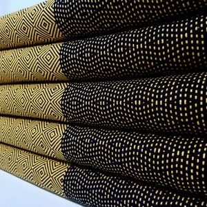 May include: A stack of four black and gold patterned towels. The towels have a geometric design with a diamond pattern and a smaller dot pattern.