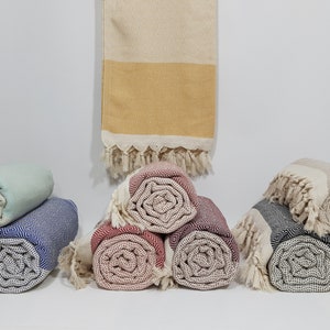 K&ouml;nnte beinhalten: Eine Sammlung von aufgerollten t&uuml;rkischen Handt&uuml;chern in verschiedenen Farben, darunter Blau, Grau, Rot und Beige. Die Handt&uuml;cher sind aus Baumwolle und haben einen Fransenrand.