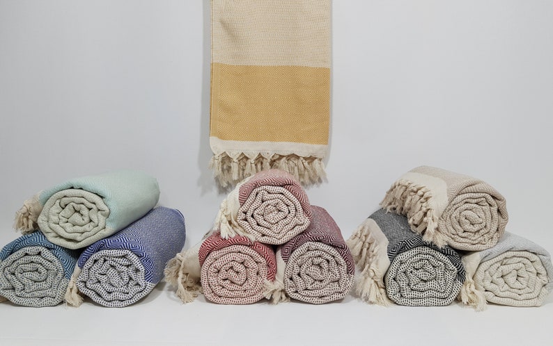 K&ouml;nnte beinhalten: Eine Sammlung von aufgerollten t&uuml;rkischen Handt&uuml;chern in verschiedenen Farben, darunter Blau, Grau, Rot und Beige. Die Handt&uuml;cher sind aus Baumwolle und haben einen Fransenrand.