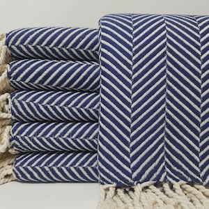 May include: A stack of blue and white striped towels with white fringe. The towels are folded and stacked on a white surface.