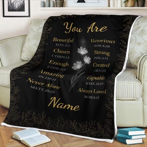 May include: A black throw blanket with gold text and floral accents. The text reads "You Are" followed by inspirational words like "Beautiful," "Victorious," and "Always Loved." A floral design and the word "Name" are also featured.