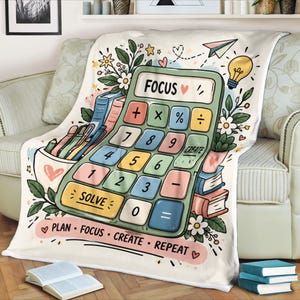 May include: A cream-coloured throw blanket featuring a large green calculator graphic with the word FOCUS, a yellow lightbulb, books, and pens. The text PLAN, FOCUS, CREATE, REPEAT is printed at the bottom with small heart and flower illustrations.