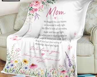 May include: A white fleece blanket featuring a floral border with pink roses, lavender, and wildflowers. The text reads: Mom, We hugged this cozy blanket we squeezed it really tight. We filled it with all our wishes, hope and love and light. We love you, Anna, James, Jordan and Kylie.