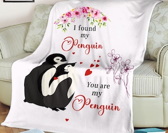 May include: A white fleece blanket featuring a penguin couple illustration. The blanket has the text "I found my Penguin, You are my Penguin" in red script, with floral and heart accents. A cozy home decor item.