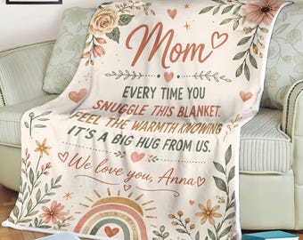 May include: Cream-colored blanket with floral and rainbow designs. The blanket has the word "Mom" in a cursive font, along with the text "Every time you snuggle this blanket. Feel the warmth knowing it's a big hug from us. We love you, Anna."