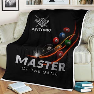 Könnte beinhalten: Schwarze Fleece-Decke mit Billard-Motiv. Die Decke zeigt ein Billardkugel-Rack, Billardkugeln und einen Billardqueue. Der Text "ANTONIO" und "MASTER OF THE GAME" ist in silbernen Buchstaben dargestellt.