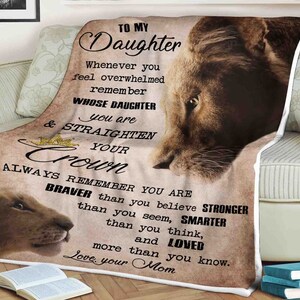 May include: A soft, beige throw blanket with a lion illustration and a message to a daughter. The text reads "To My Daughter Whenever you feel overwhelmed remember whose daughter you are & straighten your crown Always remember you are braver than you believe stronger than you seem, smarter than you think, and loved more than you know. Love, your Mom."