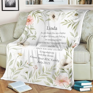 May include: A white floral blanket with a personalized message for Linda. The message reads "As you begin this new chapter in your life may you find joy in remembering the difference you have made and the lives you have touched. Congratulations and best wishes. From your RDC Family July 2025."