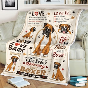 May include: A cream-colored fleece blanket featuring illustrations of Boxer dogs, paw prints, and hearts. The text reads: LOVE, LOVE IS... Wet Noses, Slobbery Kisses, Wagging Tails, LOVE LOVE BARK, Life is Better With A Boxer, FIRST THING I SEE EVERY MORNING is a BOXER who loves me.