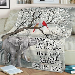 May include: A gray and white throw blanket with a floral design and two red cardinals. The blanket features a gray elephant and the text "those we love don't go away, they walk beside us every day".