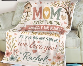 May include: A cream-colored blanket with the word "MOM" in large letters, surrounded by floral and heart designs. The blanket has text that reads "Every time you snuggle this blanket, feel the warmth knowing, it's a big hug from us, we love you! Rachel."