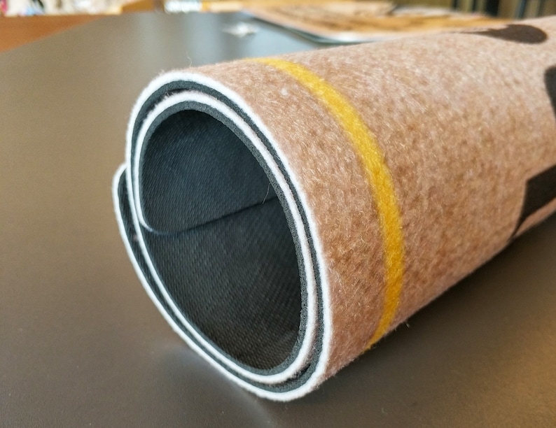 Pode incluir: Close-up de um tapete enrolado com um design marrom e bege. O tapete tem um suporte preto e uma faixa amarela ao longo da borda.