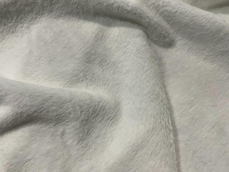 May include: Close-up of a white, soft, fluffy fabric with a slightly textured surface.