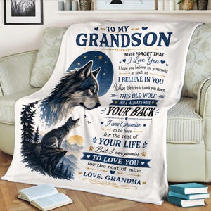 May include: A white fleece blanket featuring a large wolf head and a smaller wolf sitting on a cliffside with mountains and trees. The text reads: TO MY GRANDSON NEVER FORGET THAT I Love You I hope you believe in yourself as much as I BELIEVE IN YOU When life tries to knock you down THIS OLD WOLF WILL ALWAYS HAVE YOUR BACK I can't promise to be here for the rest of YOUR LIFE But I can promise TO LOVE YOU for the rest of mine LOVE, GRANDMA.