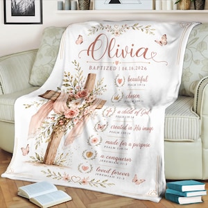 Könnte beinhalten: Eine weiße Decke mit Blumen- und Kreuzdesign. Die Decke trägt den Namen "Olivia" und das Datum "04.16.2026". Zusätzlicher Text beinhaltet "beautiful", "chosen", "a child of God", "created in His image", "made for a purpose", "a conqueror" und "loved forever".