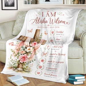Pode incluir: Cobertor branco com um design em aquarela com uma cruz de madeira adornada com rosas cor-de-rosa, vegetação e borboletas. O cobertor inclui o nome "Alisha Wilson" e texto inspirador, perfeito para um batismo ou um presente religioso.
