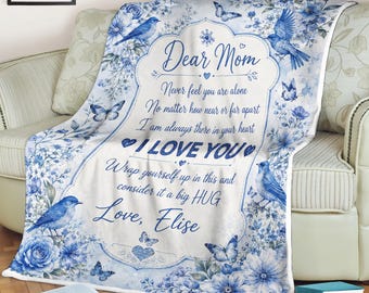 Pode incluir: Uma manta branca com um padrão floral azul, borboletas e pássaros azuis. O texto central diz: Dear Mom, Never feel you are alone, No matter how near or far apart, I am always there in your heart, I LOVE YOU, Wrap yourself up in this and consider it a big HUG, Love, Elise.