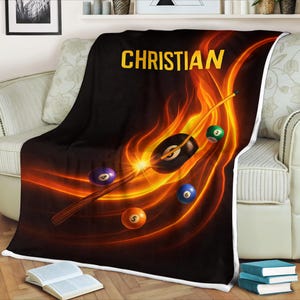 May include: Black fleece blanket with a vibrant design featuring a pool cue, billiard balls, and fiery orange and yellow flames. The name "CHRISTIAN" is displayed in bold yellow letters.
