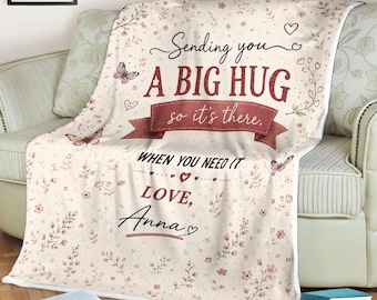 May include: A cream-colored blanket with a floral pattern and the text "Sending you a big hug so it's there. When you need it, love, Anna." The blanket features butterflies and hearts.