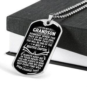 Op de afbeelding: Zilveren dogtag-hanger met een kogelketting. De hanger heeft de tekst "TO MY GRANDSON" en een liefdevolle boodschap. Gepresenteerd op een zwarte doos.