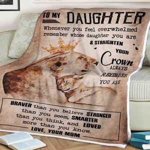 Puede incluir: Una manta de color marrón claro y marrón con una ilustración de una leona y una cría. La manta tiene un mensaje para una hija: "A mi hija, cuando te sientas abrumada recuerda de quién eres hija y endereza tu corona. Recuerda siempre que eres más valiente de lo que crees, más fuerte de lo que pareces, más inteligente de lo que piensas y amada más de lo que sabes. Con amor, Mamá."