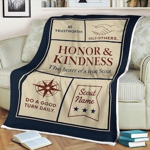 May include: A navy blue and beige blanket with text that reads "Honor & Kindness, The heart of a true Scout." The blanket also features a compass rose, the words "Do a good turn daily," and the text "Be trustworthy. Help others."