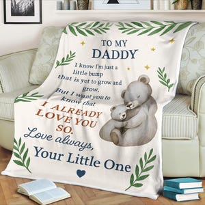 May include: White blanket with text "TO MY DADDY" and "I ALREADY LOVE YOU SO. Love always, Your Little One." Features a watercolor illustration of two hugging bears. Green leaf and star accents.