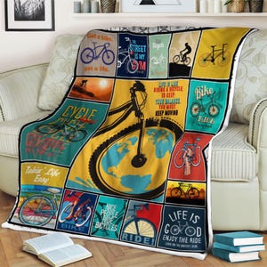 May include: A colorful bicycle-themed throw blanket with various bicycle illustrations and motivational phrases. The blanket features a collage of images in shades of blue, yellow, and red, with text like "Get a bike, get a life" and "Life is good."