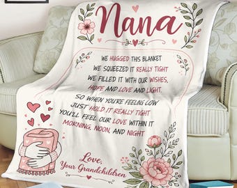 May include: A white fleece blanket featuring the word Nana in large script, floral illustrations, and a poem that reads: We hugged this blanket, we squeezed it really tight, we filled it with our wishes, hope and love and light. So when you're feeling low just hold it really tight, you'll feel our love within it morning, noon, and night. Love, Your Grandchildren.