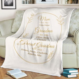 May include: A white blanket with gold text and a floral design. The text reads "Mom," "Grandma," and "Great Grandma," with names and dates. The blanket is draped over a sofa.