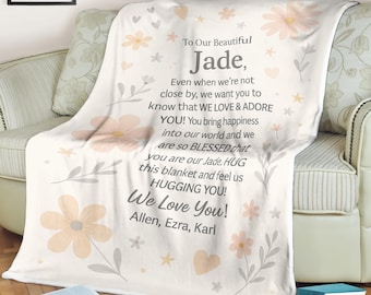 May include: A cream-colored blanket with a floral design and text that reads "To Our Beautiful Jade, We Love You!" in a script font. The blanket is draped over a sofa and features peach and gray floral accents.