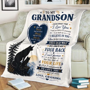 Peut inclure: Une couverture polaire blanche ornée d'un cœur bleu foncé avec un texte inspirant, une silhouette de deux loups sur une falaise surplombant des montagnes et des pins, et un message imprimé adressé à un petit-fils par une grand-mère en bleu et or.