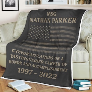Puede incluir: Una manta de franela negra y marrón con un diseño de bandera estadounidense de camuflaje. La manta tiene el texto "MSG NATHAN PARKER" y "CONGRATULATIONS ON A DISTINGUISHED CAREER OF HONOR AND ACCOMPLISHMENT 1997-2022".