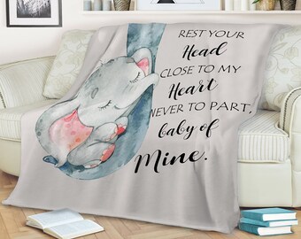 May include: A gray and white throw blanket with a watercolor illustration of a sleeping elephant. The blanket has the text "REST YOUR Head CLOSE TO MY Heart NEVER TO PART, baby of Mine."