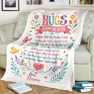 May include: A white fleece blanket featuring the text HUGS FROM HEAVEN and a poem about love and comfort. The design includes colorful floral illustrations, butterflies, and hearts in shades of pink, yellow, purple, and teal, with a space for a name.