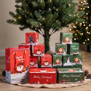 Könnte beinhalten: Eine Sammlung roter und grüner Weihnachtsgeschenkboxen und eine passende Geschenktüte mit Illustrationen von Weihnachtsmännern, Tannenbäumen und Schneemännern, mit dem Text Merry Christmas auf den Boxen und der Tüte, unter einem Baum.