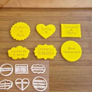 Può includere: Tagliabiscotti gialli in varie forme, tra cui un cuore, un cerchio, un rettangolo e un ovale. I tagliabiscotti sono etichettati con il testo "Battesimo di Sofia", "Leonardo & Sofia", "Leonardo 1 anno", "Leonardo 12.05.2024" e "Buon Anniversario".
