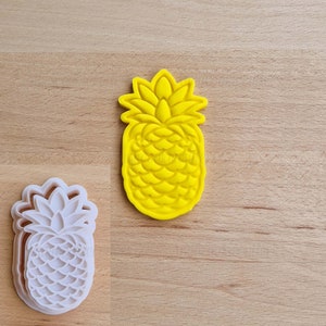 Könnte beinhalten: Zwei Ausstecher in Form von Ananas, einer gelb und einer weiß, auf einer Holzoberfläche.