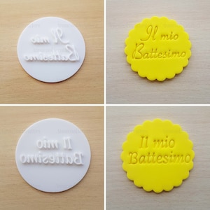 Pode incluir: Dois cortadores de biscoitos redondos brancos com o texto "Il mio Battesimo" em itálico, um com o texto invertido. Dois biscoitos redondos amarelos com o mesmo texto, um com o texto invertido.