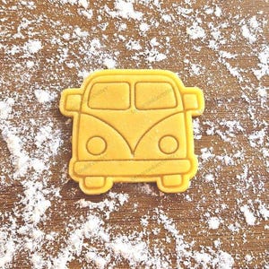 Può includere: Un tagliapasta giallo a forma di furgone Volkswagen vintage. Il tagliapasta ha la parte anteriore e posteriore arrotondata, e i finestrini e i fari sono ritagliati.