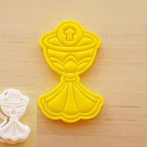 Può includere: Tagliapasta in plastica gialla a forma di calice con una croce sulla parte superiore. Il calice è su una superficie di legno.